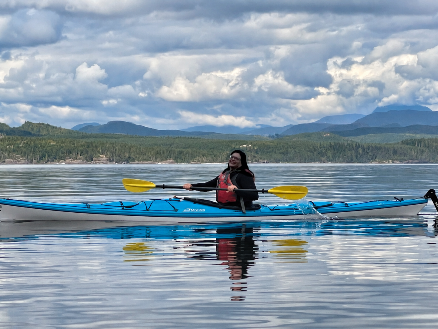 Me in a blue kayak, with calm water, forest and mountains all around